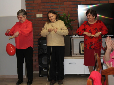 Zdjęcie przedstawia trzy seniorki biorące udział w zabawie – nawijanie balonowego serduszka na sznurku na drążek.