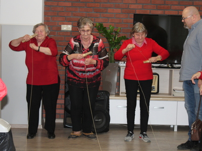 Zdjęcie przedstawia kolejne trzy seniorki biorące udział w zabawie – nawijanie balonowego serduszka na sznurku na drążek.