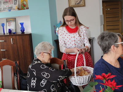 2.	Na zdjęciu znajduje się dziewczynka, która trzyma koszyk i wręcza  Seniorce mydlane serce