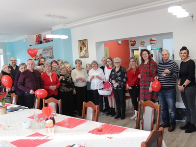 5.	Zdjęcie grupowe wykonane na sali głównej  Domu Dziennego Pobytu, przedstawiające Seniorów wraz z wolontariuszami oraz Dyrektorem MGOPS.