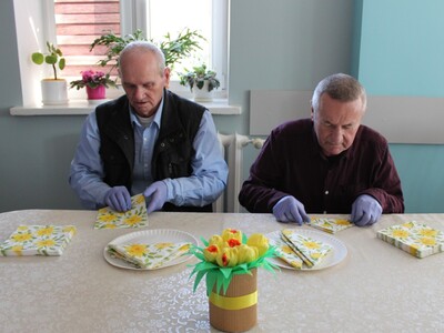 5)	Zdjęcie przedstawia dwóch seniorów składających serwetki na wielkanocny stół.