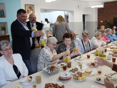 1)	Zdjęcie przedstawia burmistrza miasta Sompolna oraz dyrektora mgops w Sompolnie wręczających upominki seniorom z domu dziennego pobytu podczas wielkanocnego śniadania.