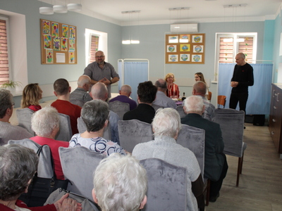 2)	Zdjęcie przedstawia dyrektora mgops zapraszającego na przedstawienie teatralne. Przed nim dużo osób siedzących