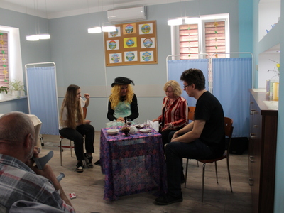 4)	Na fotografii czwórka aktorów siedzących przy stoliku na którym stoi karafka, kieliszki i talerzyki.