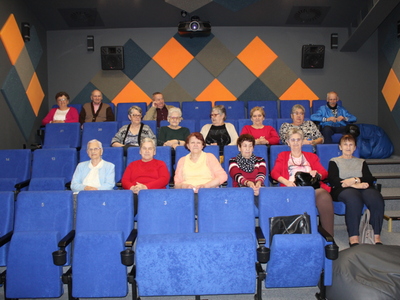 Zdjęcie wykonana w sali kinowej kina za rogiem. Przedstawia seniorów siedzących na niebieskich fotelach.