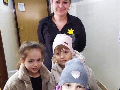 6)	Na fotografii pracownica mgops z przypiętym żonkilem oraz w towarzystwie trójki dzieci.