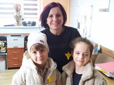 7)	Na zdjęciu pracownica mgops z żonkilem i w towarzystwie dwójki dziewczynek.