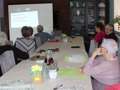 1)	Zdjęcie wykonane na sali głównej Domu Dziennego Pobytu Senior+ w Sompolnie. Przedstawia uczestników DDP uczestniczących w webinarium na temat cyberbezpieczeństwa.
