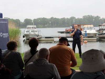 1.	Zdjęcie przedstawia policjanta stojącego nad jeziorem ślesińskim, który przemawia do grupy seniorów.