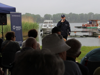 2.	Zdjęcie przedstawia policjanta stojącego nad jeziorem ślesińskim, który przemawia do grupy seniorów.