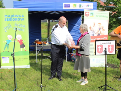 13. Zdjęcie przedstawia burmistrza wręczającego seniorce, która zajęła pierwsze miejsce w konkursie plastycznym główną nagrodę.