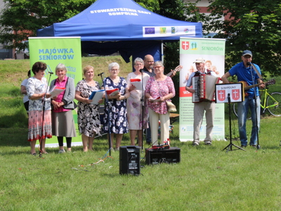 2. Fotografia przedstawia  występ seniorów z zespołu muzycznego „Wiecznie Młodzi”, którzy akompaniamencie gitary i akordeonu śpiewają piosenki.