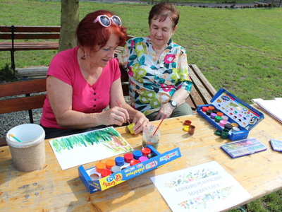 6. Zdjęcie wykonane w parku, przedstawia dwie seniorki malujące pracę plastyczną podczas konkursu przeprowadzonego na Majówce Seniorów.