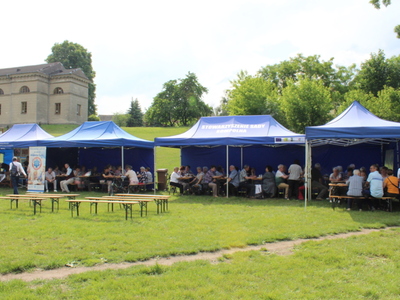 8. Zdjęcie wykonane w parku przy ulicy 11 Listopada w Sompolnie. Przedstawia namioty pod którymi siedzą seniorzy podczas majówki. W tle po lewej stronie kościół ewangelicki