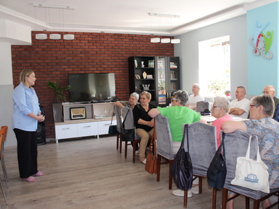 1)	Zdjęcie wykonane w sali głównej domu dziennego pobytu senior+ w Sompolnie. Przedstawia kobietę – panią adwokat podczas prelekcji dla seniorów