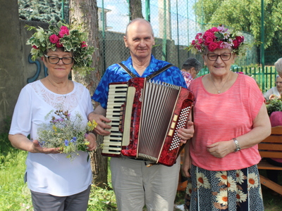 3)	Zdjęcie przedstawia mężczyznę z akordeonem oraz dwie kobiety w wiankach pozujących do zdjęcia.