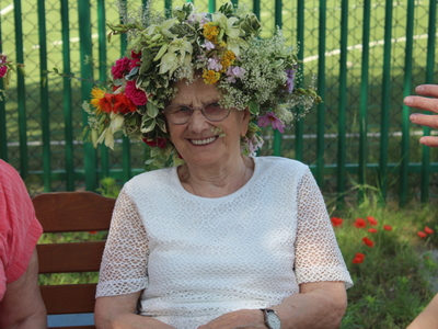 4)	Na fotografii starsza kobieta w białej bluzce i wianku pozuje do zdjęcia.