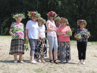 8)	Fotografia przedstawia grupę seniorek wraz z opiekunką pozujące do zdjęcia we wiankach.