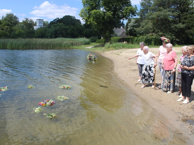 9)	Na fotografii grupa kobiet rzucająca wianki na jezioro. W tle pałac w Lubstowie.