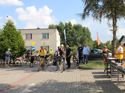 3)	Na zdjęciu uczestnicy rajdu parkujący swoje rowery na parkingu MGOPS. Po prawej stronie pracownicy ośrodka przygotowujący posiłki z grilla.