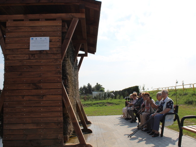 2. Zdjęcie przedstawia Seniorów siedzących na ławce przy tężni solankowej