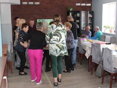 4)	Zdjęcie przedstawia seniorów wraz z opiekunami tańczących w kółku.