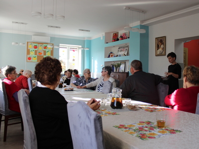 Na fotografii osoby starsze siedzące przy stole. Po prawej stronie doradca obywatelski – kobieta prowadząca prelekcję.