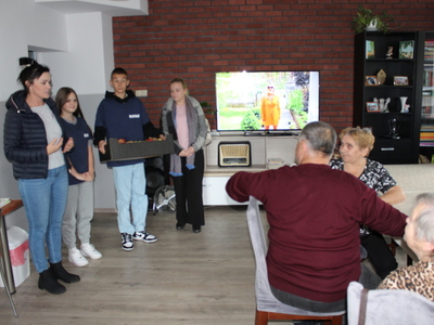 Na zdjęciu uczniowie wraz z opiekunkami przekazują skrzynkę jabłek seniorom z DDP.