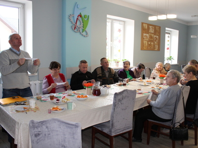 Zdjęcie wykonane na sali głównej Domu Dziennego Pobytu dla osób starszych w Sompolnie. Przedstawia seniorów czytających sentencje z kartek przyczepionych do cukierków.