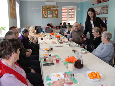 Na fotografii seniorzy częstujący się cukierkami z kapelusza.