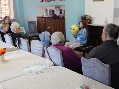 Zdjęcie przedstawia dziewczynkę występującą na sali głownej DDP oraz Seniorów stanowiących publiczność