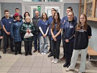 1)	Zdjęcie wykonane na korytarzu szkoły w Mąkolnie. Przedstawia wolontariuszy i seniorów na zdjęciu grupowym.