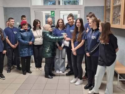 2)	Zdjęcie grupowe na którym jedna z seniorek wręcza wolontariuszom worek z cukierkami.