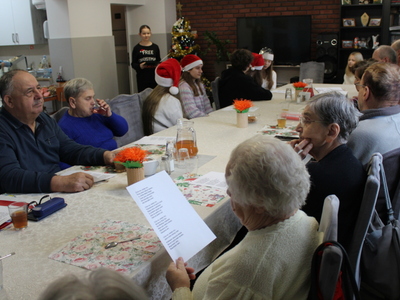 4. Na pierwszym planie zdjęcia znajdują się seniorzy, którzy słuchają występu muzycznego uczennicy.