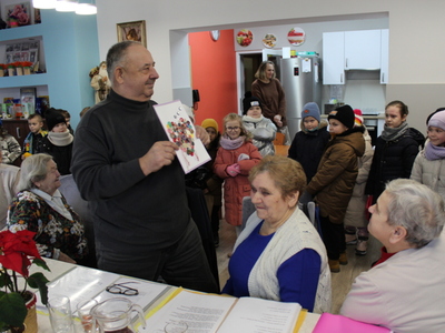 2)	Na zdjęciu dzieci i seniorzy. Jeden z nich prezentuje kartkę z życzeniami.