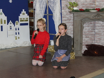4)	Na zdjęciu dwie dziewczynki klęczące na ziemi. Z lewej strony zimowa inscenizacja, a z prawej kominek.