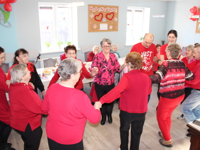 Na fotografii seniorzy i opiekunowie tańczący w kole.