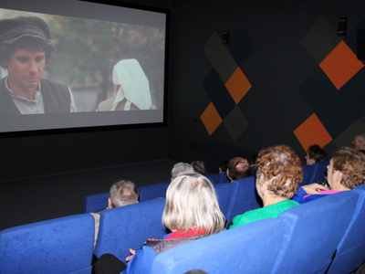 Zdjęcie wykonane podczas trwania seansu. Przedstawia ekran kina i seniorów oglądających film.