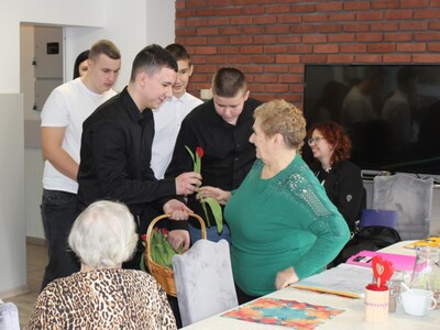 2. Zdjęcie przedstawia uczniów wręczających Seniorce kwiat tulipana