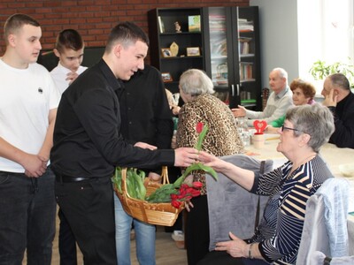 3. Na zdjęciu widzimy chłopców podchodzących do Seniorki by wręczyć jej kwiatka.
