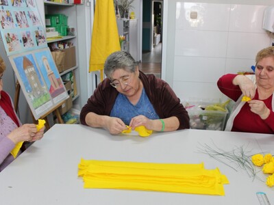 Zdjęcie wykonane w pracowni plastycznej. Przedstawia trzy seniorki robiące kwiaty w krepiny