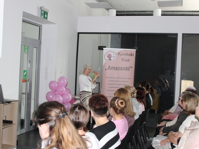 6. Zdjęcie przedstawia słuchaczy oraz Panią z Konińskiego Klubu Amazonki, która przy użyciu fantomu piersi demonstruje sposoby wykonywania samobadania piersi.