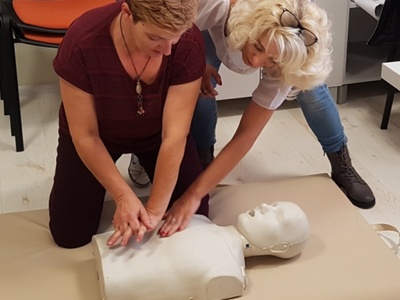 Na zdjęciu znajdują się dwie kobiety. Na podłodze leży tułów manekina. Jedna z kobiet uczy drugą techniki masażu serca.