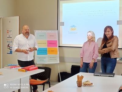Zdjęcie wykonane podczas trwania warsztatów dla rodziców. Przedstawia dyrektora miejsko - gminnego ośrodka pomocy społecznej w Sompolnie oraz dwie kobiety, które prowadziły "Szkołę dla rodziców". W tle ekran rzutnika.