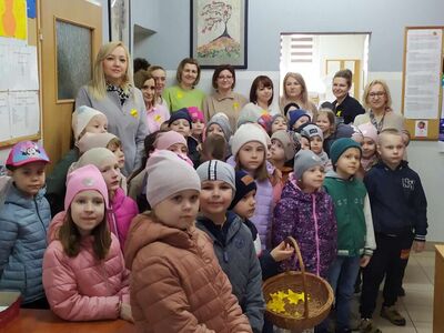 Fotografia wykonana w Miejsko – Gminnym Ośrodku Pomocy Społecznej w Sompolnie. Ukazuje pracowników i dzieci z koszem papierowych żonkili.