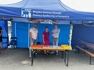 2)	Zdjęcie przedstawia pracowników MGOPS w Sompolnie stojących pod namiotem. Przed nimi stoisko MGOPS.