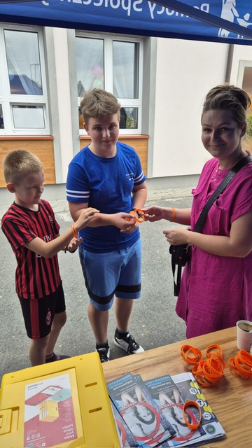 1)	Na fotografii pracownica Miejsko – Gminnego Ośrodka Pomocy Społecznej w Sompolnie podczas pikniku rodzinnego który odbył się w Sycewie. Rozdaje dzieciom opaski silikonowe z nadrukiem „Stop przemocy!”