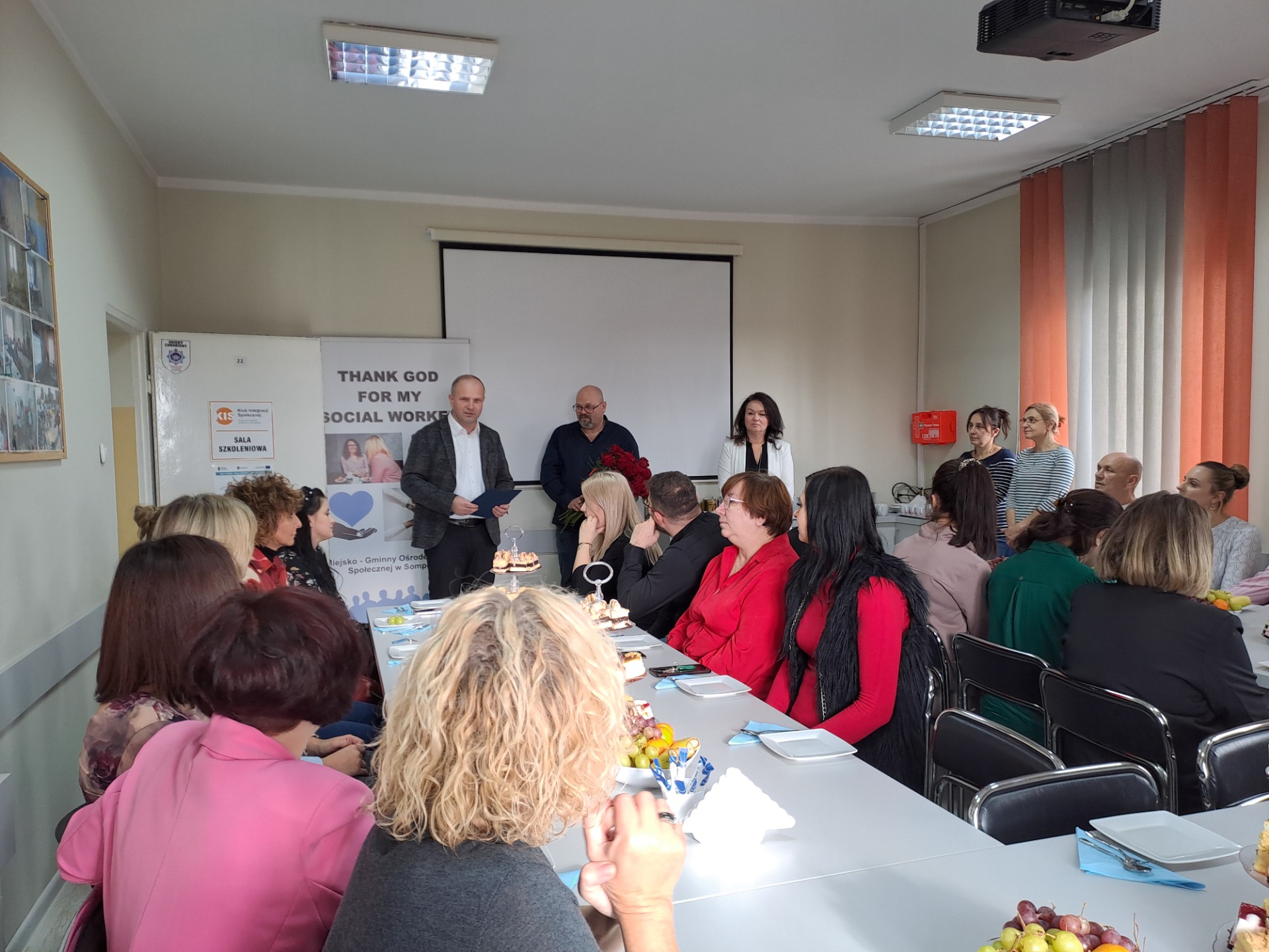 Zdjęcie wykonane w sali wykładowej M-GOPS w Sompolnie. Przedstawia Pana Waldemara Marciniaka - burmistrza miasta Sompolna wraz z Panią Anetą Niestrawską – sekretarz gminy składających życzenia Panu Tomaszowi Majewskiemu - dyrektorowi oraz pracownikom mgops w Sompolnie.