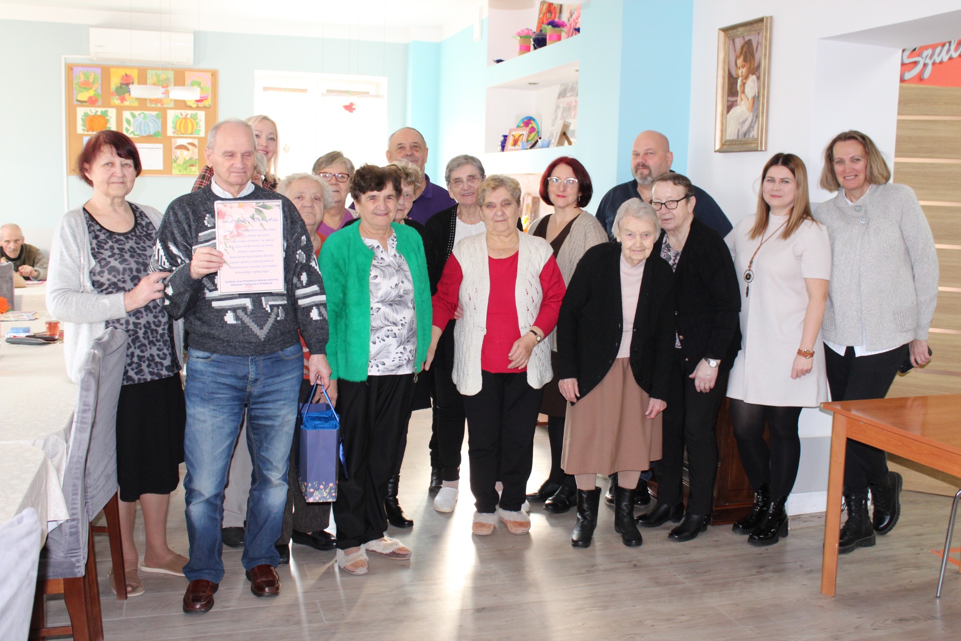 1)	Zdjęcie grupowe wykonane w Domu Dziennego Pobytu. Przedstawia seniorów, delegację z biblioteki oraz pracowników mgops w Sompolnie.