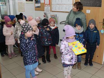 Zdjęcie wykonane w Miejsko – Gminnym Ośrodku Pomocy Społecznej w Sompolnie. Przedstawia grupę przedszkolaków wraz z nauczycielką. Jedna z dziewczynek stoi z laurką dla pracowników.